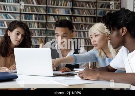 Four multi ethnic student studying in library using laptop Stock Photo