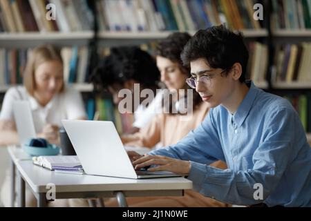 Student guy wear glasses studying in library using laptop Stock Photo