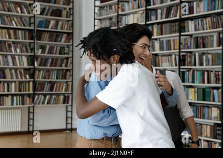 Happy multi ethnic teenagers students hugging standing in library Stock Photo