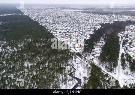 Aerial winter view high above few houses in the valley, surrounded by pine tree forest