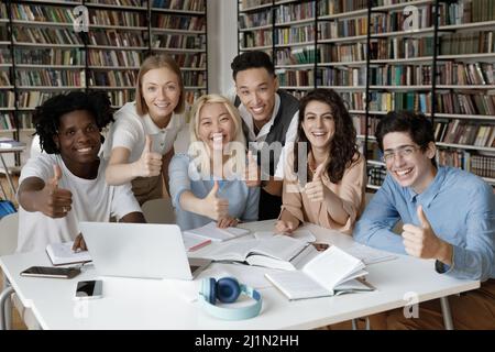 Multiracial students gather in library showing thumbs up at camera Stock Photo