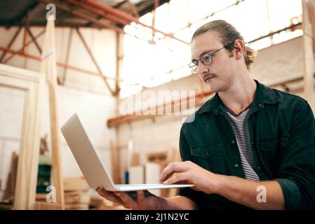 Being tech savvy always comes in handy in business. Cropped shot of a handsome young carpenter using a laptop while working inside his workshop. Stock Photo