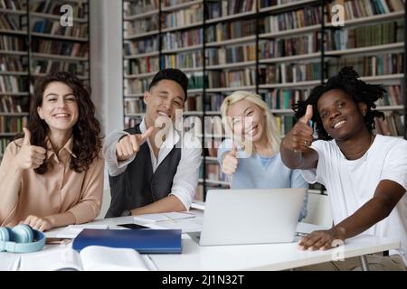 Multiethnic students showing thumbs up sit at table in library Stock Photo