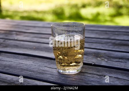 Glass with sparkling lemonade on a wooden table in a garden café in summer. Stock Photo