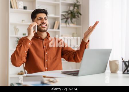 Angry Arab man talking on cell phone using laptop Stock Photo