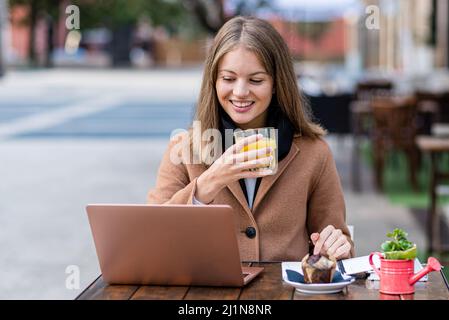 young student having breakfast, freelance caucasian woman reading documents on laptop and sips orange juice, telecommuting concept and online trading Stock Photo