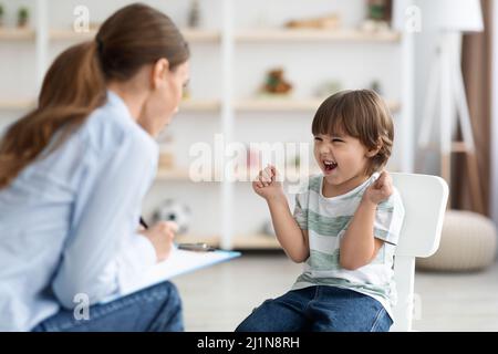 Little furious kid screaming at woman psychologist, denying communication and treatment during consultation, free space Stock Photo