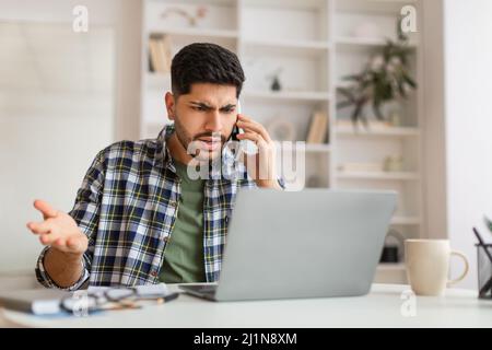 Angry Arab man talking on cell phone using laptop Stock Photo
