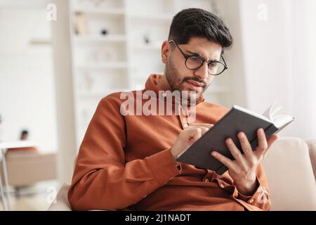 Focused Arab man in glasses trying to read book Stock Photo
