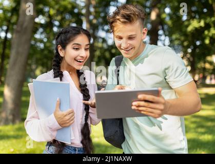 University lifestyle concept. Student guy showing digital tablet to girlfriend, looking at test results outdoors Stock Photo
