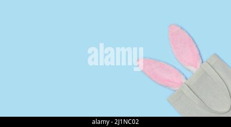 Banner. Pink Easter bunny ears sticking out of Reusable textile bag on a blue background. Happy Easter minimal concept. An Easter card with a copy of Stock Photo
