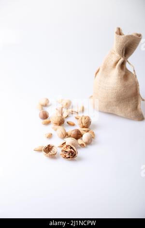 Assorted nuts in the shell on a white background: walnuts, pecans, almonds, macadamia. Nuts in a burlap bag. Selective focus, close-up. Place for text Stock Photo