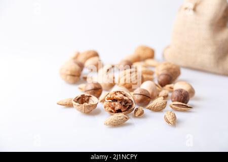 Assorted nuts in the shell on a white background: walnuts, pecans, almonds, macadamia. Nuts in a burlap bag. Selective focus, close-up. Place for text Stock Photo