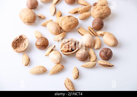 Assorted nuts in the shell on a white background: walnuts, pecans, almonds, macadamia. Selective focus, close-up. Stock Photo