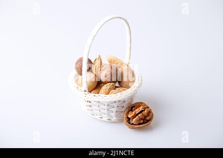 Assorted nuts in the shell on a white background: walnuts, pecans, almonds, macadamia. Nuts in a basket. Selective focus, close-up. Place for text. Stock Photo