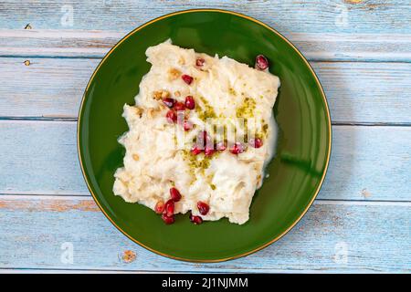 Gullac dessert on wooden background. Traditional Ramadan dessert. Güllaç dessert decorated with pistachio and pomegranate. Turkish cuisine delicacies. Stock Photo