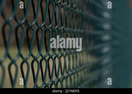 Close up of a woven green plastic coated iron wire fence in a field with the focus left of center. Background image Stock Photo