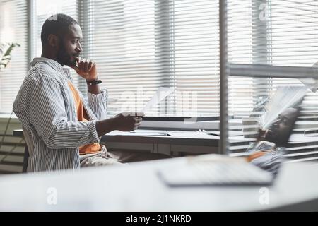Minimal side view portrait of smiling African American businessman working at home and analyzing documents with data, copy space Stock Photo