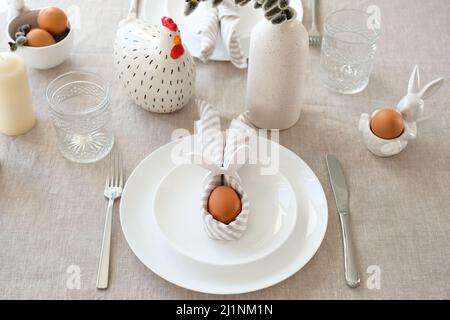 Easter table setting with egg in Easter bunny napkin on plate. Easter table serving. Stock Photo