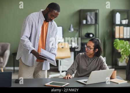 Portrait of African American man talking to Asian colleague asking advice on project in office Stock Photo