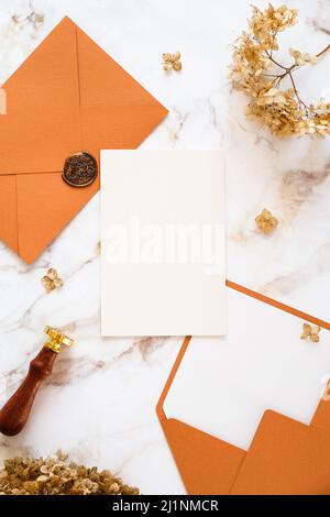 Autumn flat lay composition with wedding invitation card mockup, golden rings, envelopes, dried flowers on marble table. Wedding stationery set Stock Photo