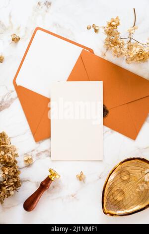 Wedding stationery set top view. Blank wedding invitation card mockup, envelopes, golden rings, dried flowers on marble table. Stock Photo