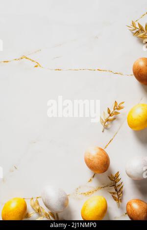 Elegant Easter vertical flat lay composition. Luxury Easter eggs with golden branches on marble table. Stock Photo