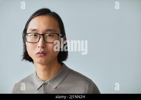 Minimal close up portrait of young Asian businessman wearing glasses and looking at camera while standing against light blue background in studio, cop Stock Photo