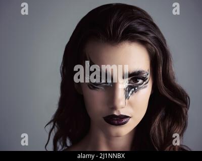 Come over to the dark side. Studio shot of an attractive young woman wearing bold makeup. Stock Photo