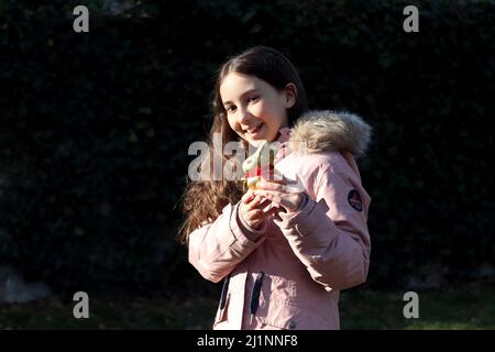 Geneva, Switzerland - 03 07 2022 Happy young girl with golden easter bunny on hands. Girl is celebrating Easter gift outdoor in park or forest.Toddler Stock Photo