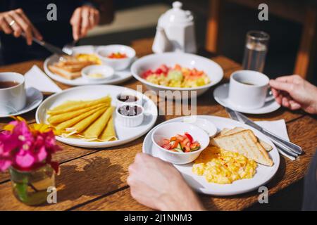 Breakfast for couple in tourist resort. Scrambled eggs and toast bread, pancakes, fruit and drinks on wooden table. Stock Photo