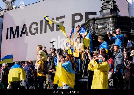 London UK, 26th March 2022. Thousands of people join a Stand with Ukraine march  and vigil in central London in protest against the Russian invasion. Marchers gather at Piccadilly Circus where Yoko Ono’s ‘IMAGINE PEACE’ artwork is displayed on the screens. Stock Photo