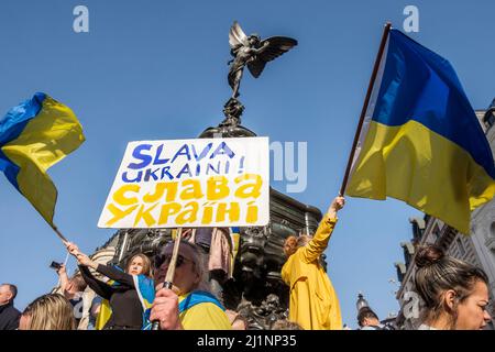 London UK, 26th March 2022. Thousands of people join a Stand with Ukraine march  and vigil in central London in protest against the Russian invasion. Marchers wave flags beneath the monument in Piccadilly Circus. Stock Photo
