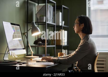 Side view portrait of Asian software designer using computer while working late at home office, copy space Stock Photo