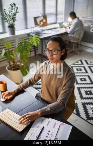 Vertical portrait of Asian software developer using computer while working late at office Stock Photo