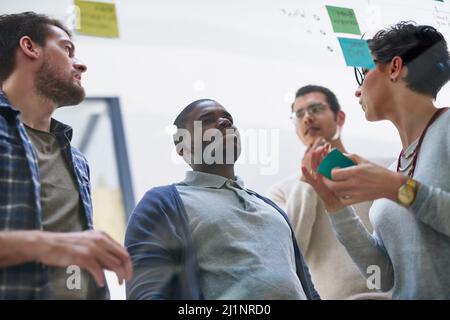 Planning with one sticky note at a time. Shot of a group of designers brainstorming with notes on a glass wall in an office. Stock Photo