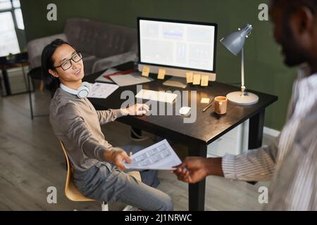 High angle view at businessman handing documents to Asian colleague while meeting in office Stock Photo