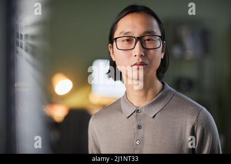 Clean front view portrait of Asian young man looking at camera while standing in office late in evening, copy space Stock Photo