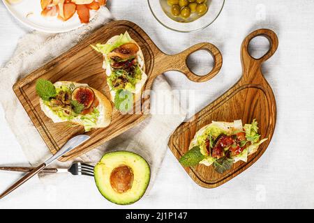 Tasty prosciutto sandwich, figs, cream cheese, avocado and herbs. Delicious and healthy breakfast. Top view Stock Photo