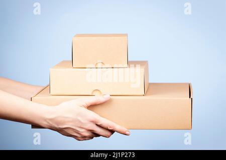 Stack of cardboard boxes in female hands. Blank brown parcel boxes on light blue background. Packaging, shopping, free shipping, delivery concept Stock Photo