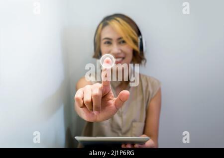 Close-up touching point on virtual screen touched by Asian woman finger while using tablet and headphone on white background with copy space. Music cr Stock Photo