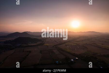Aerial view of Colorful sunset over mountain and harvested paddy fields in farmland at countryside Stock Photo