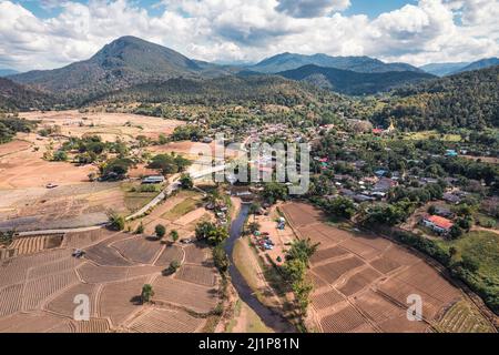 Aerial view of tranquil local village with river flowing through among the valley and rice plantation on dry season in countryside at Muang Kong, Chia