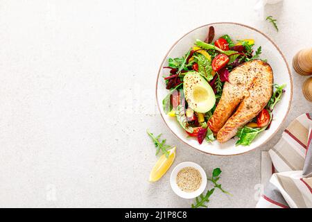Salmon fish steak grilled, avocado and fresh vegetable salad with tomato, bell pepper and leafy vegetables. Top view Stock Photo