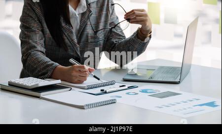 Business woman are taking notes and using calculators and laptops on a white table. Accounting concepts Stock Photo
