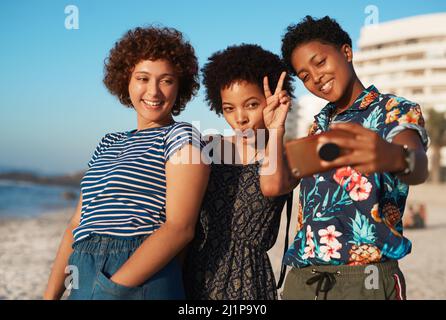 Strike a pose ladies. Shot of three attractive young women laying down on the beach and taking selfies together during the day. Stock Photo