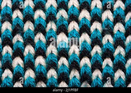 Synthetic knitted fabric with pattern elements of blue, black and white yarns close up. Multicolor patterned knitted fabric texture. Background Stock Photo
