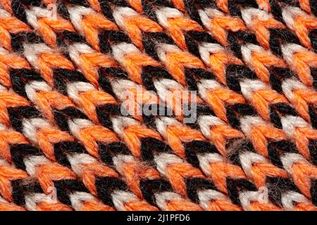 Synthetic knitted fabric with pattern elements of red, black and white yarns close up. Multicolor patterned knitted fabric texture. Background Stock Photo