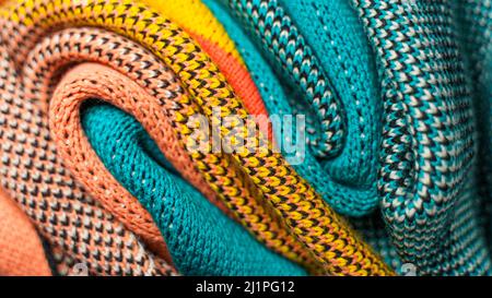 Twisted folds of colorful knitted fabrics of winter clothes with different structures and textures. Smooth shapes background. Smooth folded multi colo Stock Photo