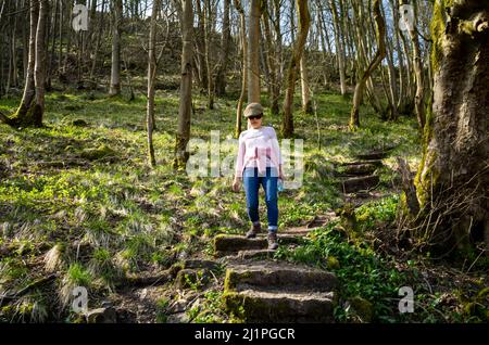 AVietnamese woman walks down a steep wooded path at Cressbrook Dale in the Peak District Nation al Park, Derbyshire, UK Stock Photo